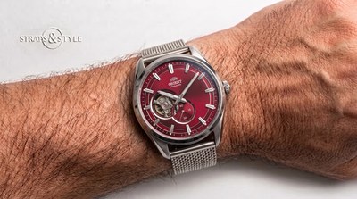Orient open-heart automatic with a fumé ruby-red dial, balance-wheel cut-out at nine and a small-seconds counter on a Straps&Style mesh bracelet