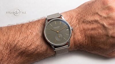 NOMOS Glashütte Orion with an olive-grey dial, gold-toned baton markers, a date at three and a small-seconds counter at six on a Straps&Style mesh bracelet