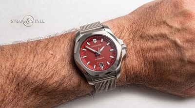 Victorinox rugged field watch with a textured brick red dial, luminous indices and a faceted steel bezel on a Straps&Style mesh bracelet