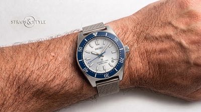 Seiko diver with a silvery white dial, a blue rotating dive bezel and a date between four and five on a Straps&Style mesh bracelet
