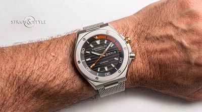 Michel Herbelin diver with a black ribbed dial, orange-accented dive bezel, day-date at three and a steel mesh bracelet on the wrist