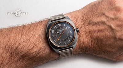 Hermès H08 cushion-case watch with grained anthracite dial, orange inner track and date between four and five on a Straps&Style mesh bracelet