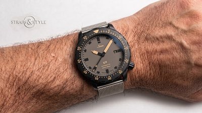 Sinn U1 diver with a matte taupe olive dial, tan luminous indices, a black dive bezel and a date at three on a Straps&Style mesh bracelet