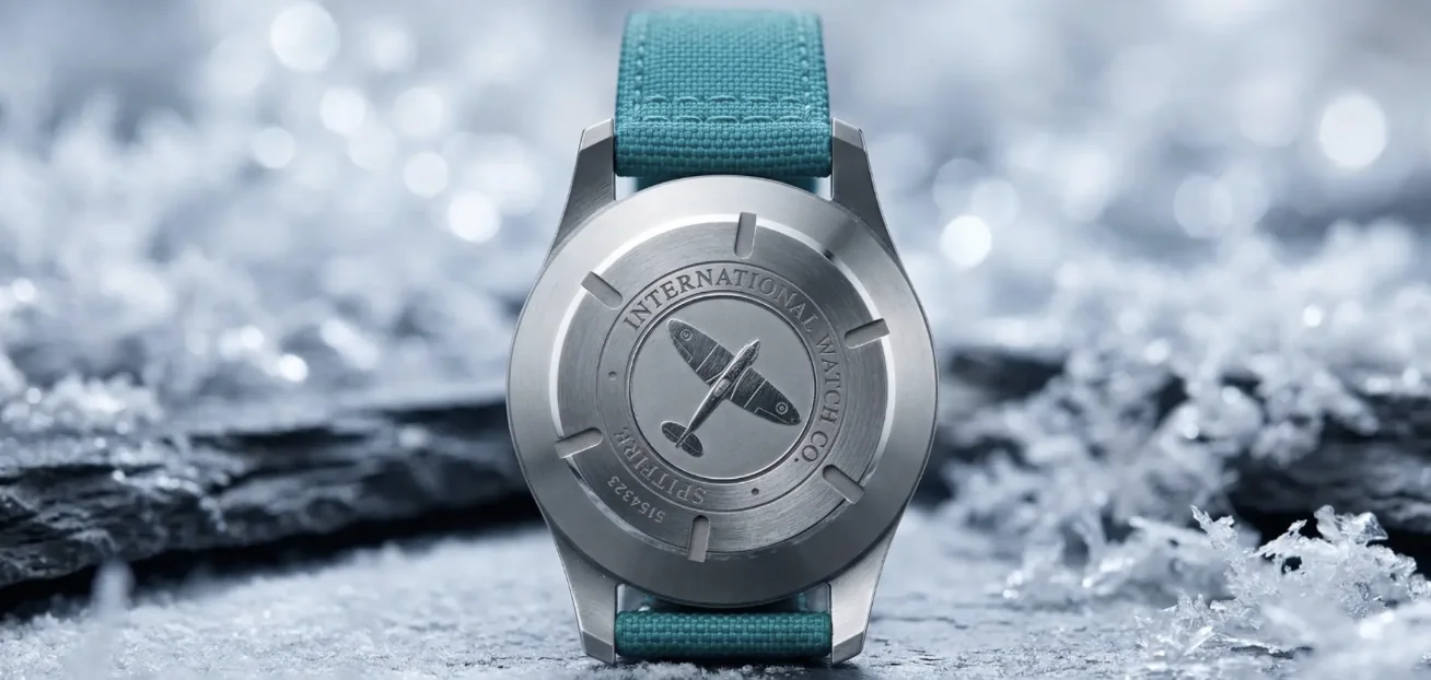 Engraved steel caseback of a watch fitted with a turquoise sailcloth nylon strap resting on frost