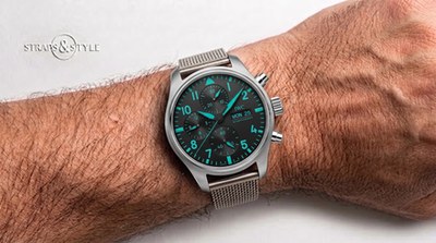 IWC Schaffhausen chronograph with a matte black dial, teal luminous numerals and day-date at three on a Straps&Style mesh bracelet