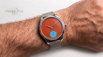 H. Moser & Cie watch with a matte orange dial and pale blue small-seconds subdial at six on a Straps&Style mesh bracelet